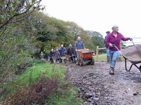 A convey of volunteers are depositing stone clippings from a wheel barrow and layering and levelling it down to make a footpath.