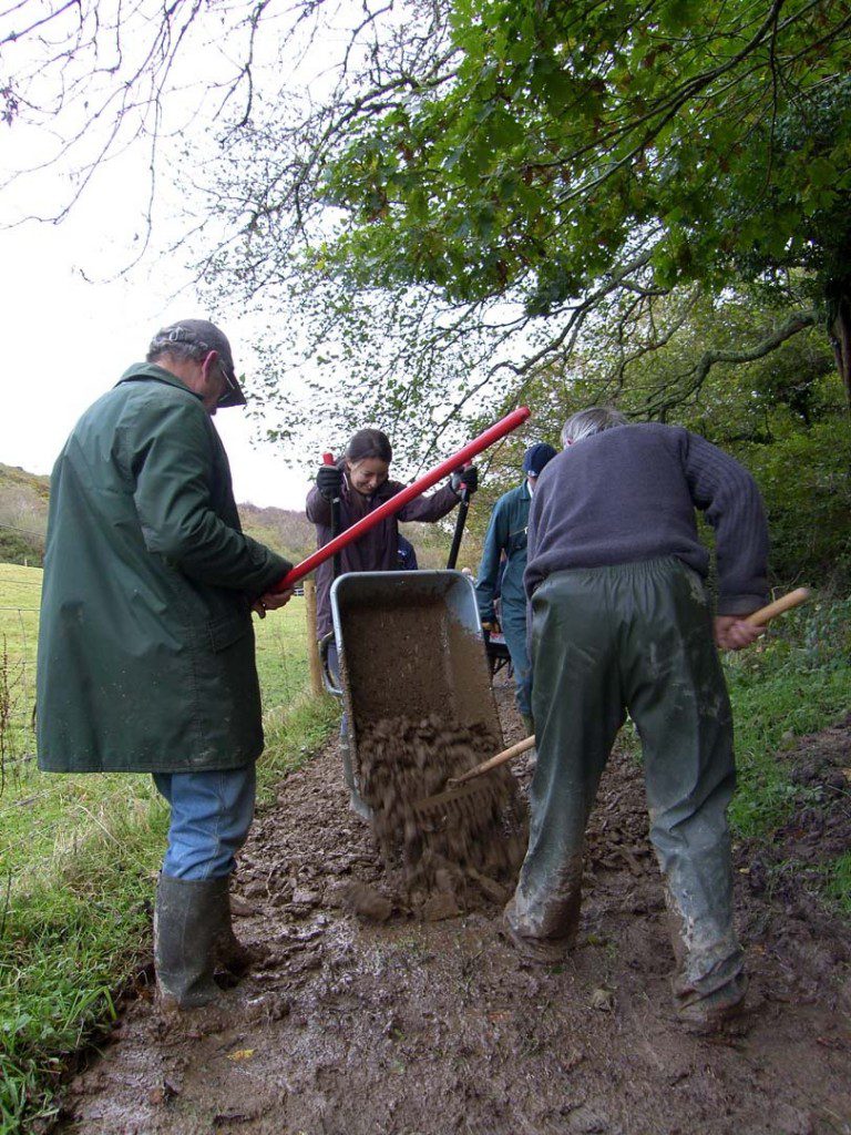 Volunteers are depositing stone clippings from a wheel barrow and layering and levelling it down to make a footpath.